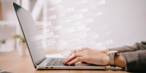 Sideview of young woman's hands typing on laptop with email icon graphics flying out of the screen