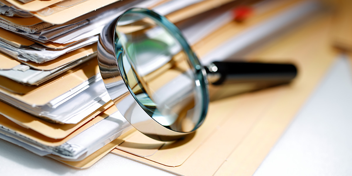 Magnifying glass leaning against a large stack of full file folders