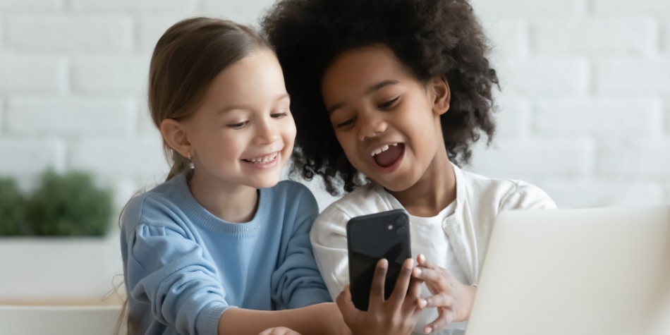 Two children looking at a mobile phone and laptop