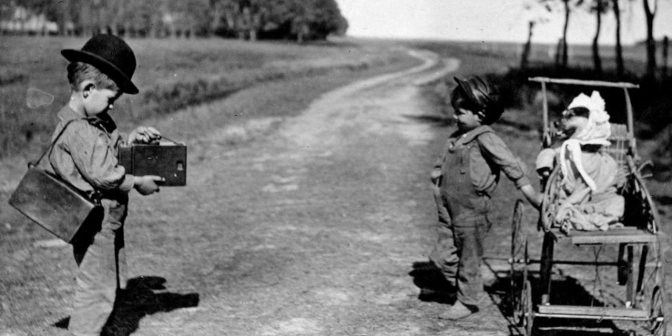 Child taking photo of another child with a dog in a stroller