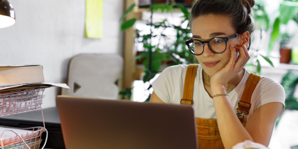 Woman with glasses at desk looking at laptop