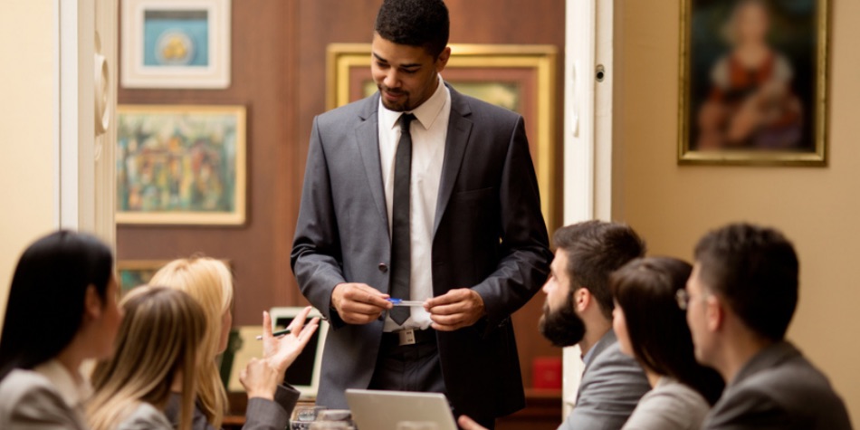 Man standing and speaking in front of a group at conference table