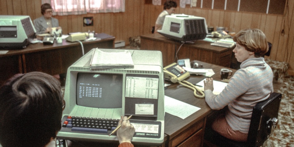 Several people in an office setting with large 1980s computers